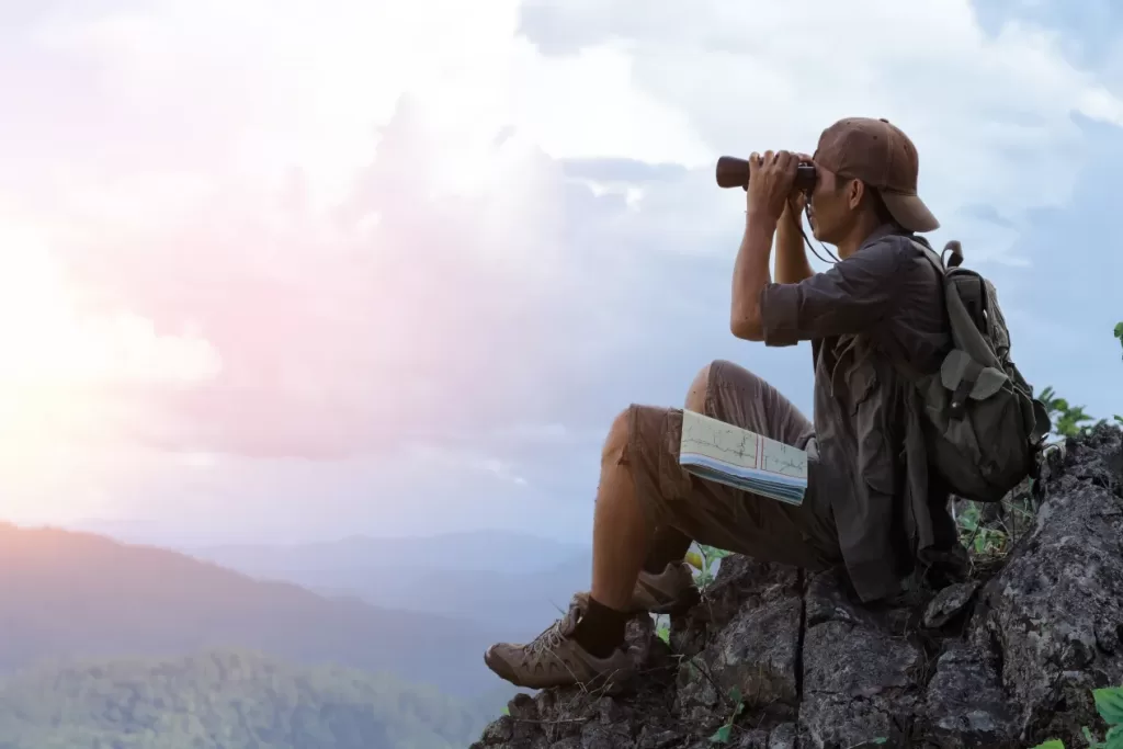 Person with binoculars sitting on a mountain slope
