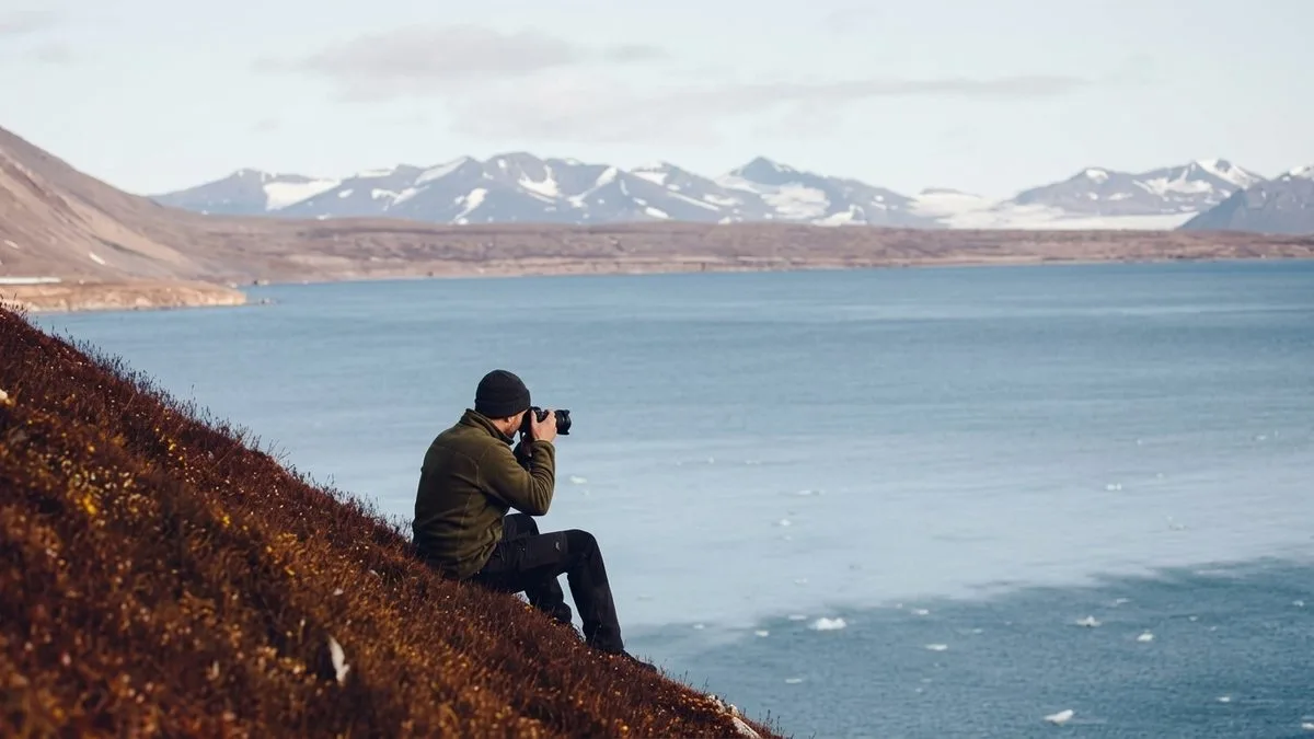Travel photographer with camera and gear photographing a mountain lake