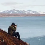 Travel photographer with camera and gear photographing a mountain lake