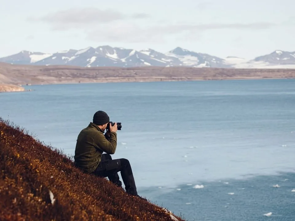 Travel photographer with camera and gear photographing a mountain lake