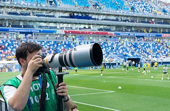 Sports photographer with big telephoto lens at soccer match